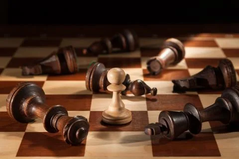 Chess. A white pawn stands on a chessboard among the lying black figures. Stock Photos