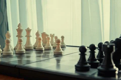 Chessboard with figures near the window with started game Stock Photos