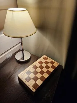 Chessboard on the table illuminated by lamp light in a dark room Stock Photos