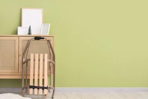 Chest of drawers with frames and sled near green wall in room Stock Photos