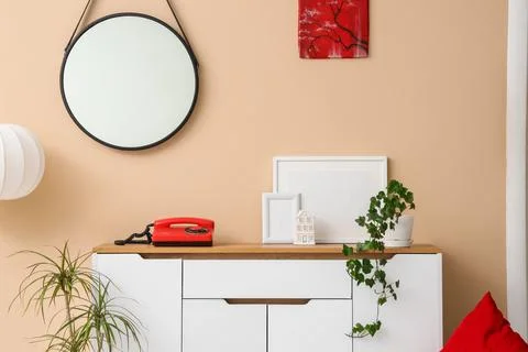 Chest of drawers with telephone, blank frames and plants near beige wall in r Stock Photos
