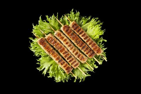 Chevapchichi, meat appetizer on a black background. Lettuce leaves complement Stock Photos