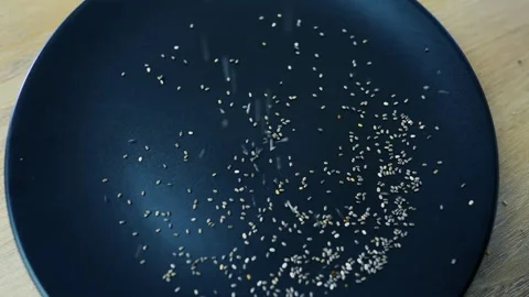 Chia seeds falling onto a dark plate on a wooden surface Stock Footage 320726762