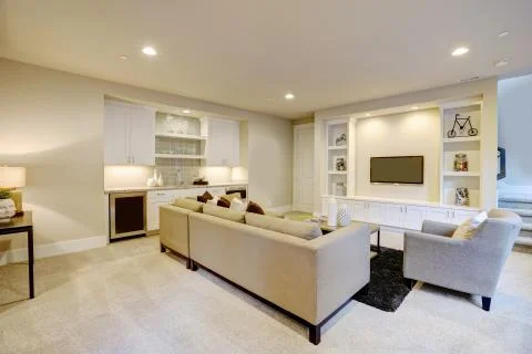Chic basement features a gray sectional facing a white built-in tv cabinet Stock Photos