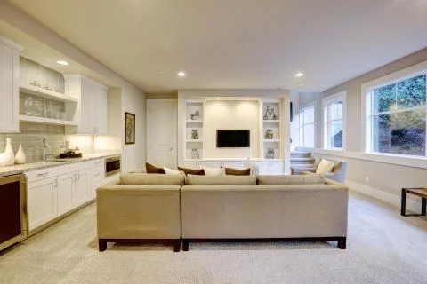 Chic basement features a gray sectional facing a white built-in tv cabinet Stock Photos