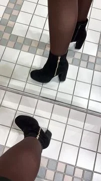 A chic black suede ankle boot with a gold zipper is reflected in a mirror on  Stock Photos