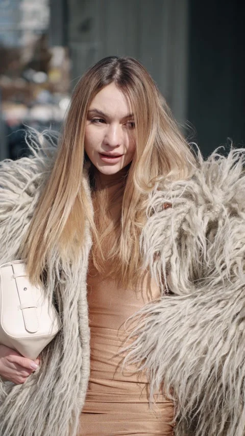 A chic look featuring a shaggy gray fur coat, nude outfit, and white handbag Stock Footage 303012520