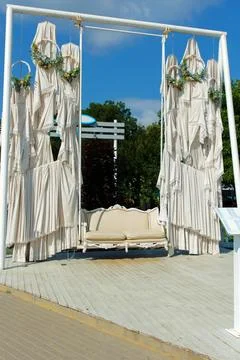 Chic swing with white leather trim set in park. White fabric decor with wre.. Stock Photos