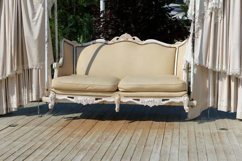 Chic swing with white leather trim set in park in summer. White fabric deco.. Stock Photos