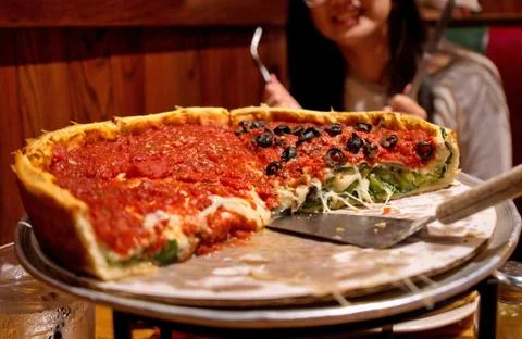 A Chicago style deep dish pizza being eaten by hungry and smiling customers. Stock Photos