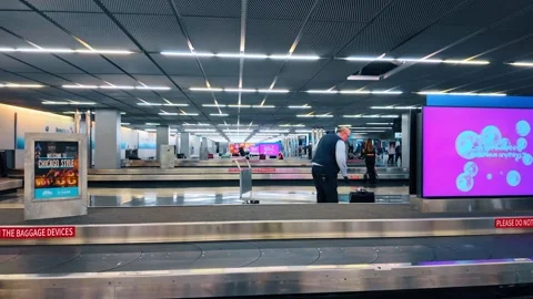 Chicago, USA, 7 May 2026: Man with luggage cart at empty baggage carousel, Stock Footage 336339038