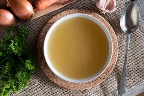 Chicken bone broth with vegetables in the background, top view Stock Photos
