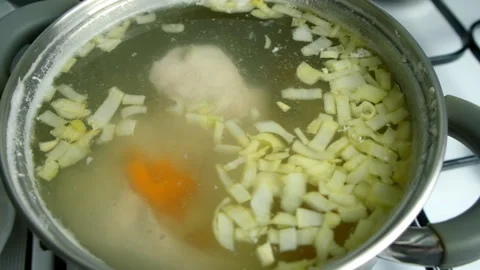 Chicken broth simmering with vegetables in pot cooking on gas stove on kitchen. Video stock 312451392