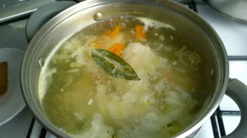 Chicken broth simmering with vegetables in pot cooking on gas stove on kitchen. Stock Footage 312451721