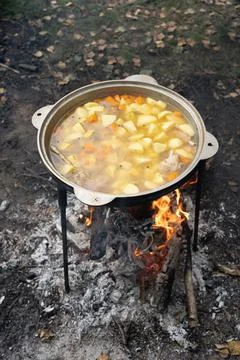 Chicken chowder made of chicken wings and vegetables is cooked on a fire during Stock Photos