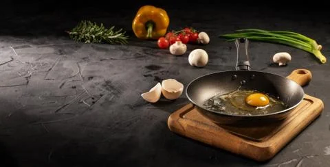 Chicken egg in empty pan surrounded by vegetarian cuisine ingredients Stock Photos