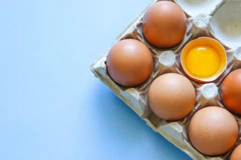 Chicken egg is half broken among other eggs. Brown eggs and egg yolk Stock Photos