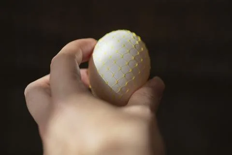 Chicken egg in hand on a dark background. Easter. yellow mesh, decoration. Stock Photos