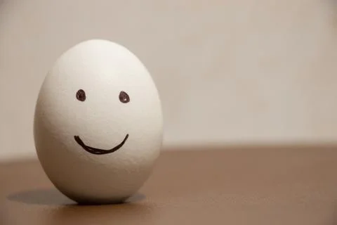 Chicken egg with a smile drawn on the table Stock Photos