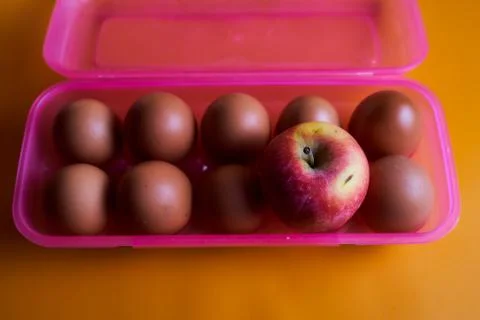 Chicken eggs with apple in plastic box on a pink background. Concept photo. Stock Photos