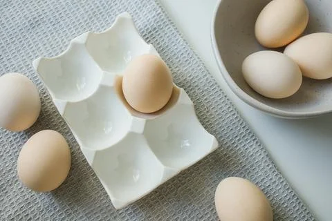 Chicken eggs in ceramic easter tray, kitchen bowl and on grey kitchen towel Stock Photos