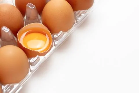 Chicken eggs in clear plastic box with egg yolk in half of eggshell on white Stock Photos