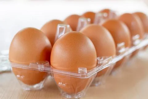 Chicken eggs in clear plastic box on wooden table. Stock Photos