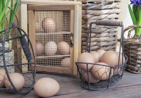 Chicken eggs in a decorative box and metal baskets on a table in front of a.. Stock Photos