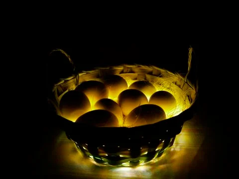 Chicken eggs in a large basket on a thin straw with an unusual light. Stock Photos