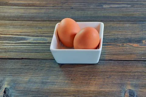 Chicken eggs in a square white clay plate on a wooden background. Side view,  Stock Photos