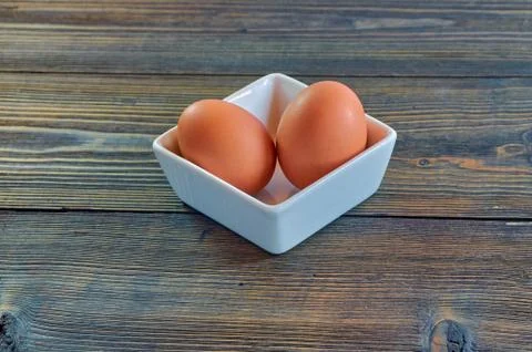 Chicken eggs in a square white clay plate on a wooden background. Side view Stock Photos