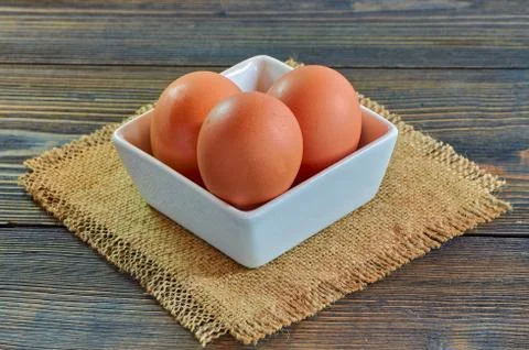 Chicken eggs in a square white clay plate on a burlap napkin, on a wooden Stock Photos
