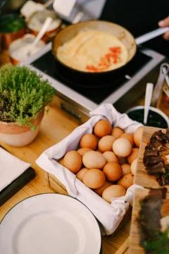 Chicken eggs, on the table in the kitchen with plates, a flower pot and a frying Stock-Fotos