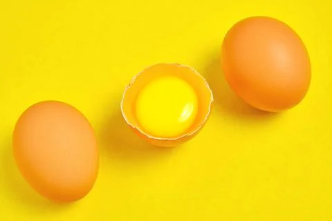 Chicken eggs on a yellow background broken with yolk. Stock Photos