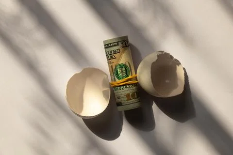 Chicken eggshell and roll of hundred dollar bills on white background in sh.. Stock Photos