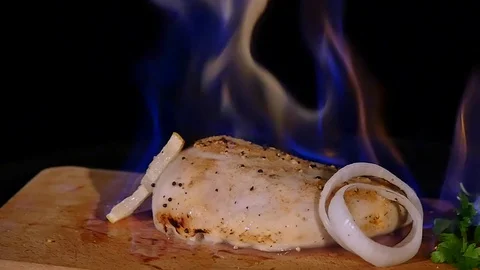 Chicken fillet in the fire on the wooden board. Barbecue meat. Dark background Stock Footage