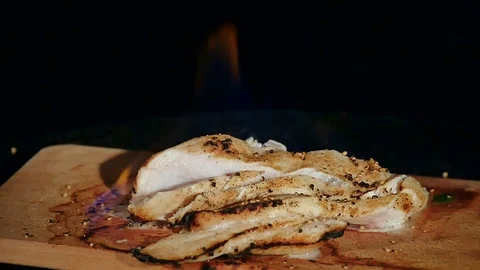 Chicken fillet in the fire on the wooden board. Barbecue meat. Dark background Stock Footage
