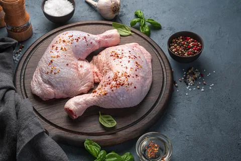 Chicken legs with pepper on a background of spices, oil and basil on a graphi Stock Photos