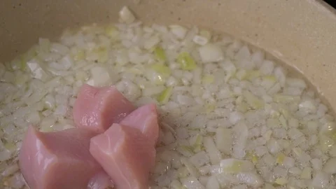 Chicken meat in cubes are being added in to the pan with frying onion. Stock Footage 128819427