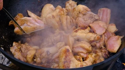 Chicken meat is stewed in a cauldron. A dish on a fire in a cauldron. The meat Stock Footage 280354858