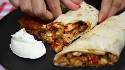Chicken pieces wrapped in tortilla bread and sauces served on black plate Stock Footage 100565459