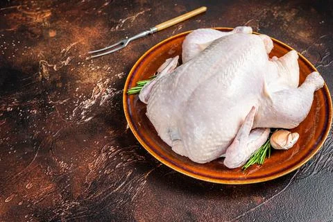 Chicken, raw poultry in a rustic plate with rosemary. Dark background. Top view Foto stock