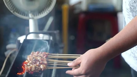 The chicken satay is grilled while turning the satay so that it is cooked Stock Footage 268515892