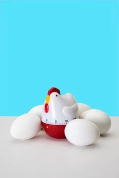 Chicken Shaped Kitchen Timer with Eggs on a White Table and Vibrant Blue Ba.. Stock Photos