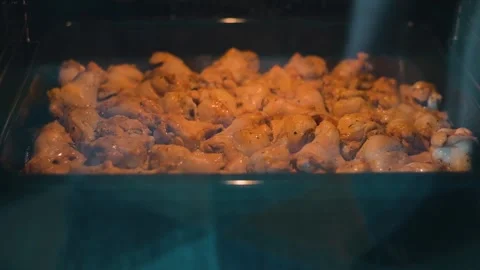 Chicken wings are placed in an oven for cooking. The light shines on the wings Stock Footage 338290465