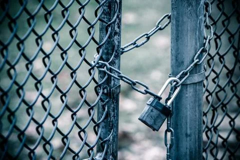 Chicken wire fence gate is locked with a chain and a lock. Toned image. Stock Photos