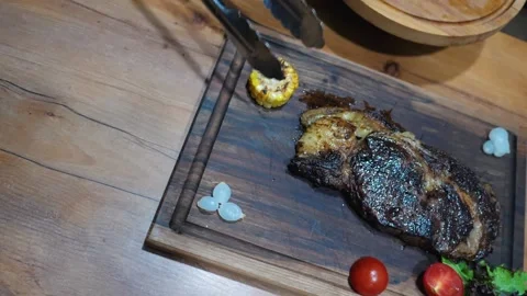 Chief serving fried steak with vegetables. grilled beef and corn 스톡 동영상 221118999