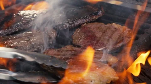 Chief using the tongs and turning the meat on the grill Stockbeeldmateriaal 108350262