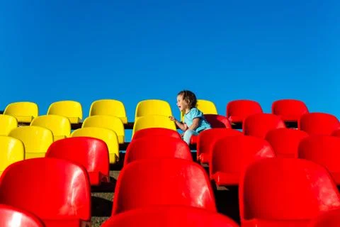 Child 3-4 years to empty stands. yellow and red seats in the open air Stock Photos