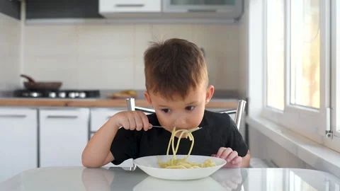 Child 6 years old boy in the kitchen eating pasta Stock Footage 144191998